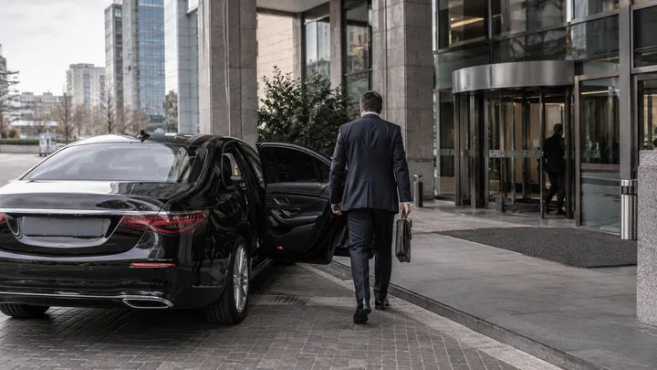 A business traveller beside a black executive car outside a modern office building